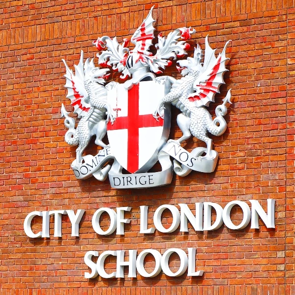 Герб школы "City of London School" на фоне красной кирпичной стены.